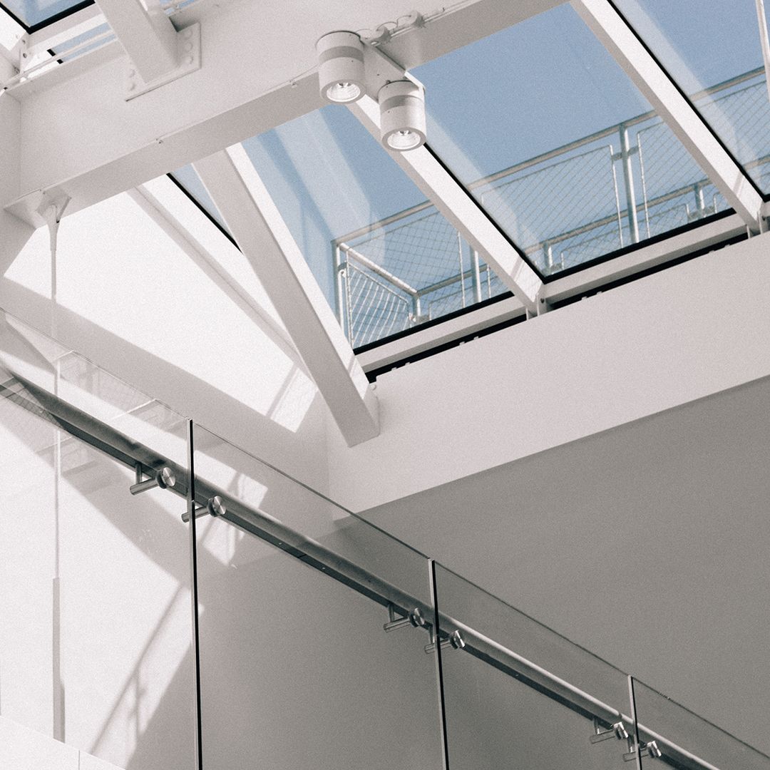 A bright interior space featuring a white steel structural frame, a glass staircase railing, and a large skylight.