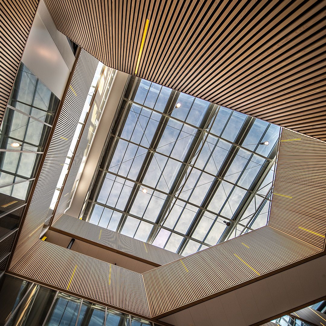 A low-angle view of a rectangular glass skylight framed by light-toned, linear wooden slat ceiling panels.