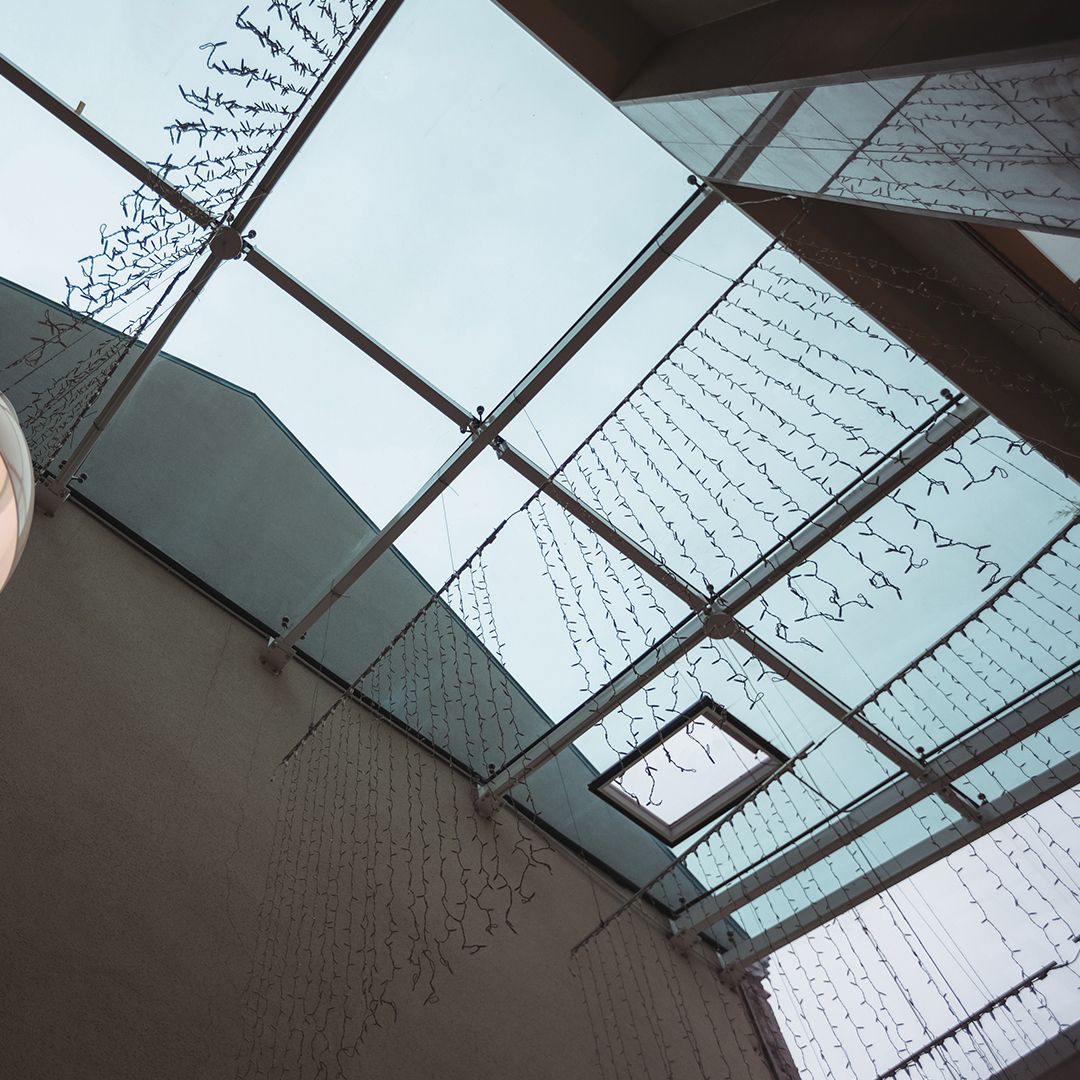 A glass skylight with a metal frame and hanging decorative string lights viewed from below against an overcast sky.