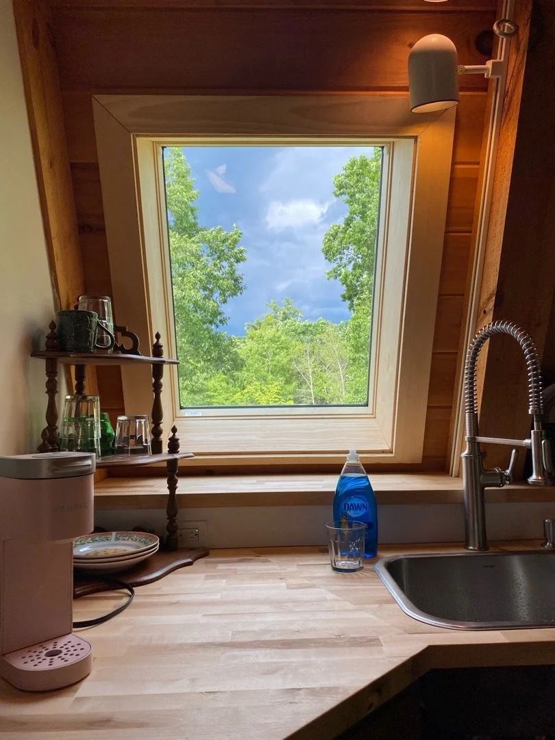 Cozy wooden kitchen with sink and window overlooking green trees and blue sky