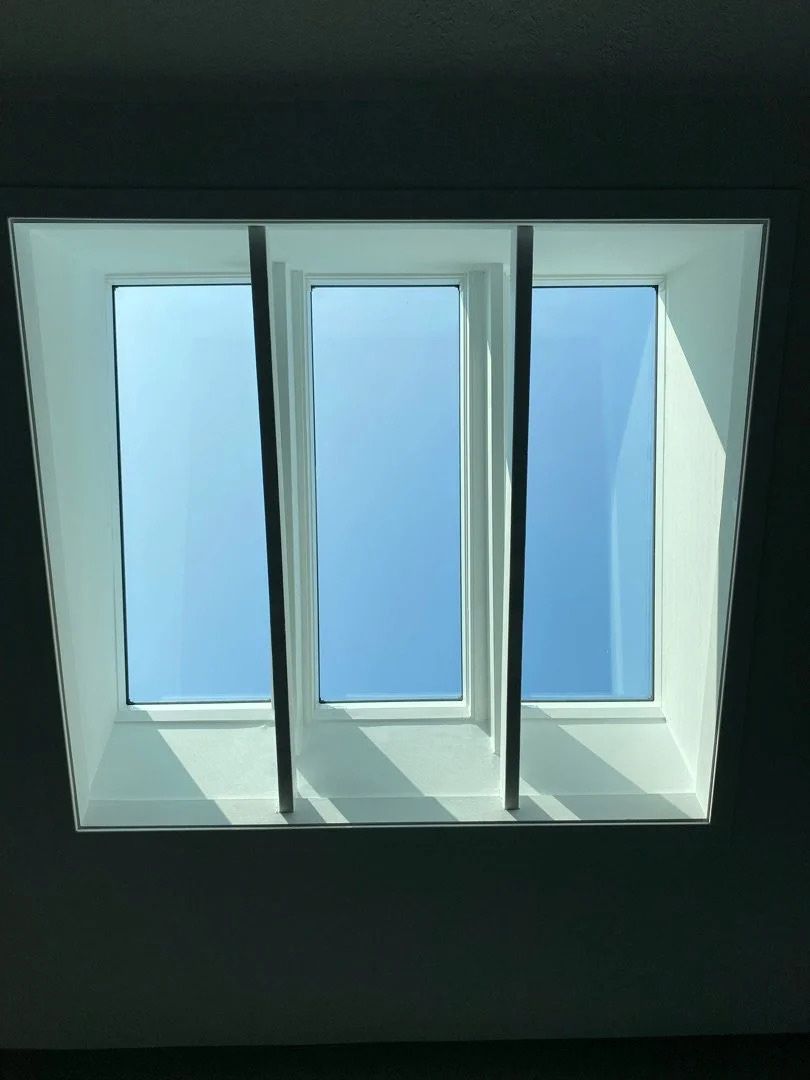 Three tall skylight windows letting in blue daylight through a white ceiling frame
