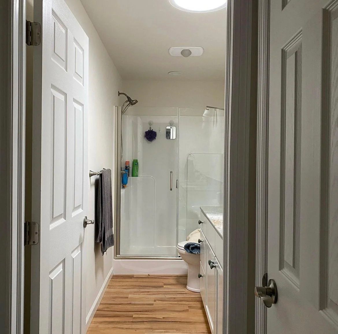 Narrow bathroom hallway with open doors, a shower, and wood-look floor.