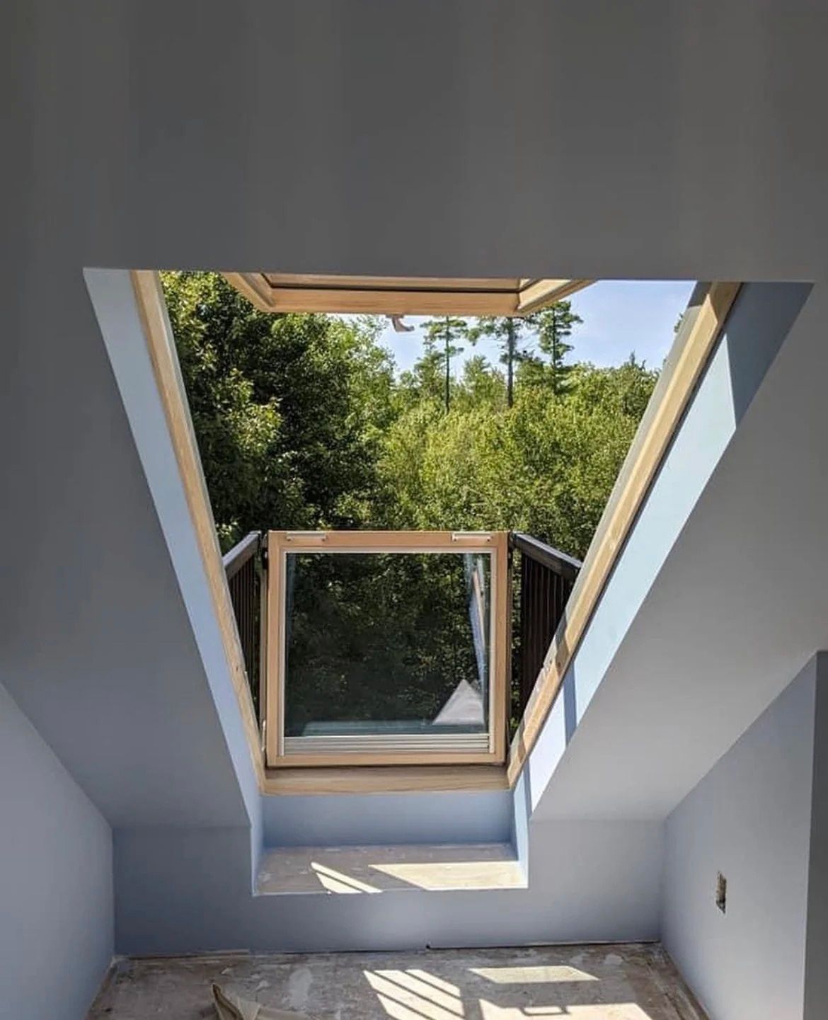 Skylight view of trees and blue sky above a room with a sloped white ceiling
