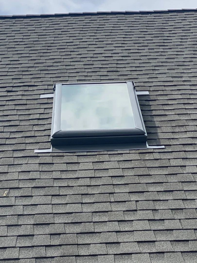 Skylight on a gray shingled roof under cloudy light