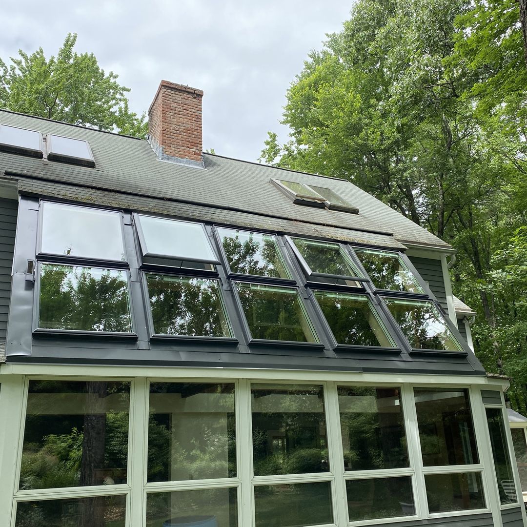 House with a sloped metal roof and large reflective windows surrounded by trees