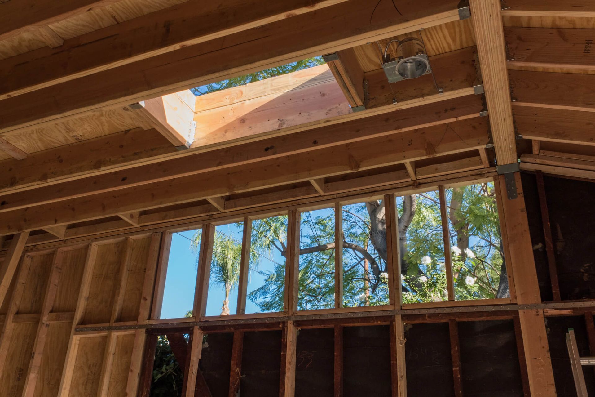 Interior of unfinished house with exposed wooden framing and a skylight opening to blue sky.