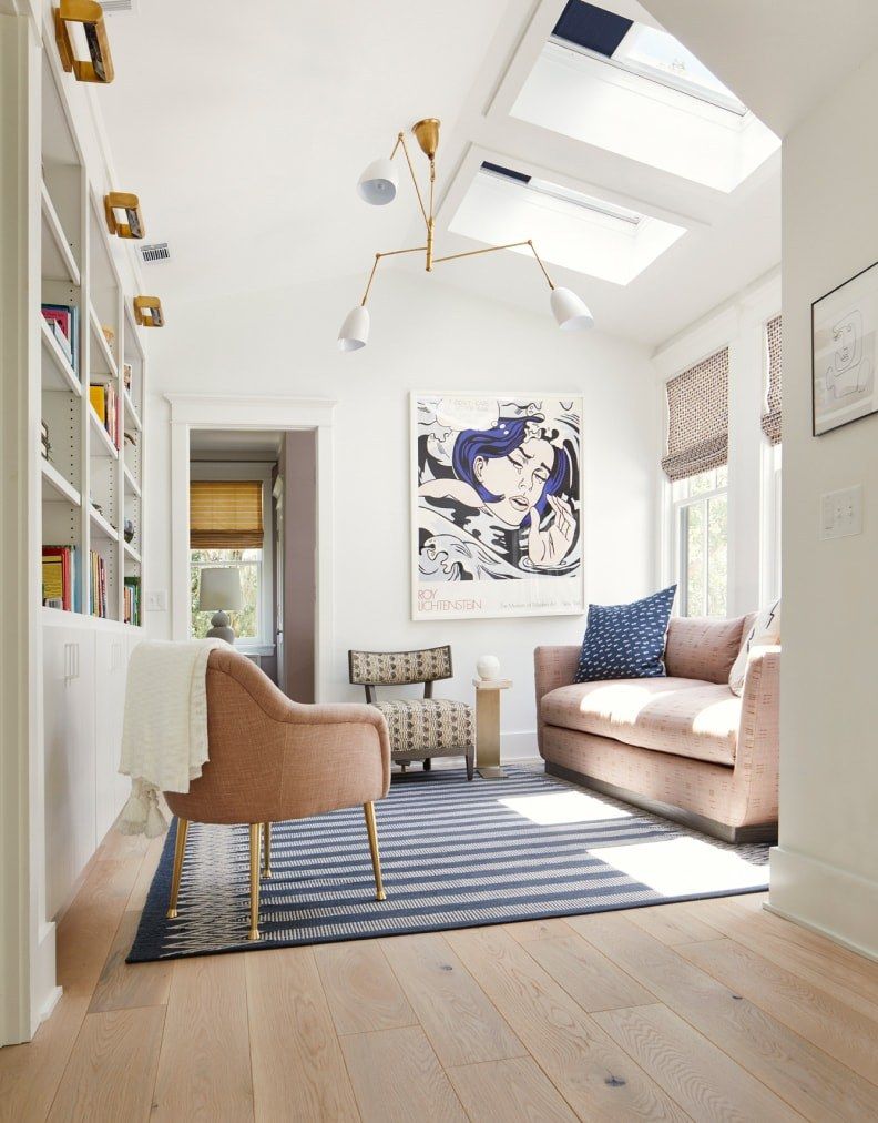 Bright modern living room with skylight, pink sofa, striped rug, and abstract wall art
