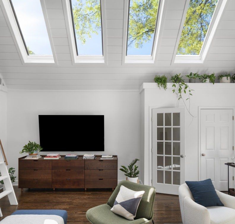 Bright living room with skylights, TV on wooden console, and green and white chairs