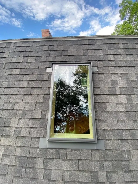 Gray shingled roof with a small skylight reflecting trees and sky