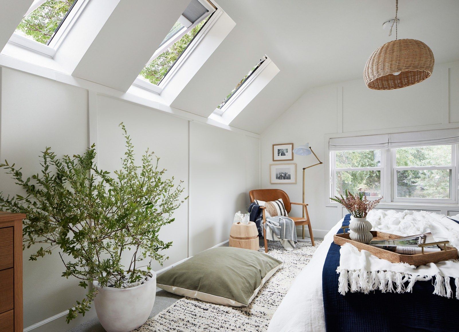 Bright attic bedroom with skylights, plants, and a bed by a window.