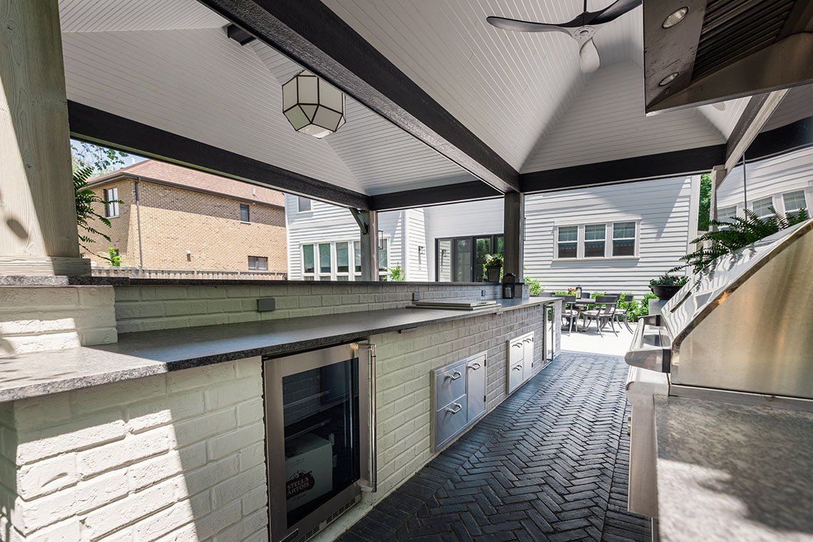 A large outdoor kitchen with a ceiling fan and a refrigerator.