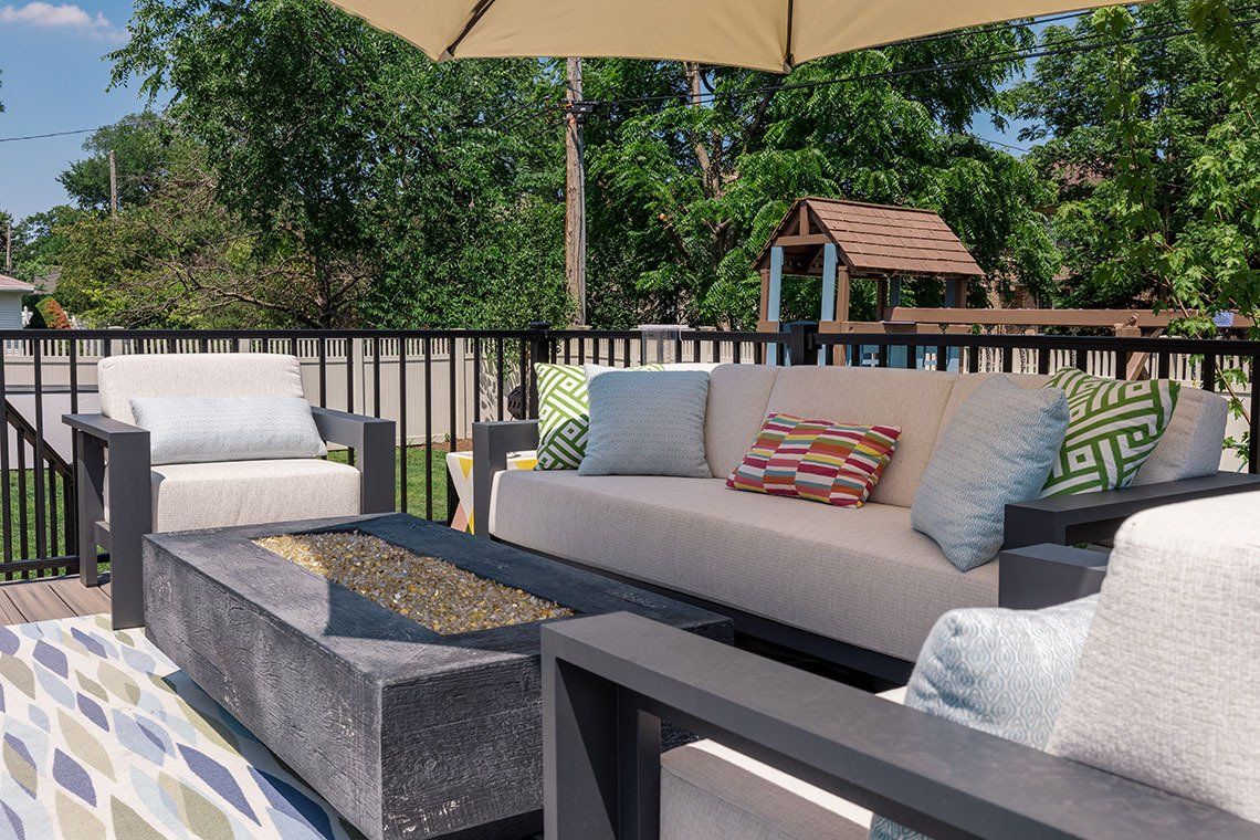 A patio with a couch , chairs , and a fire pit.