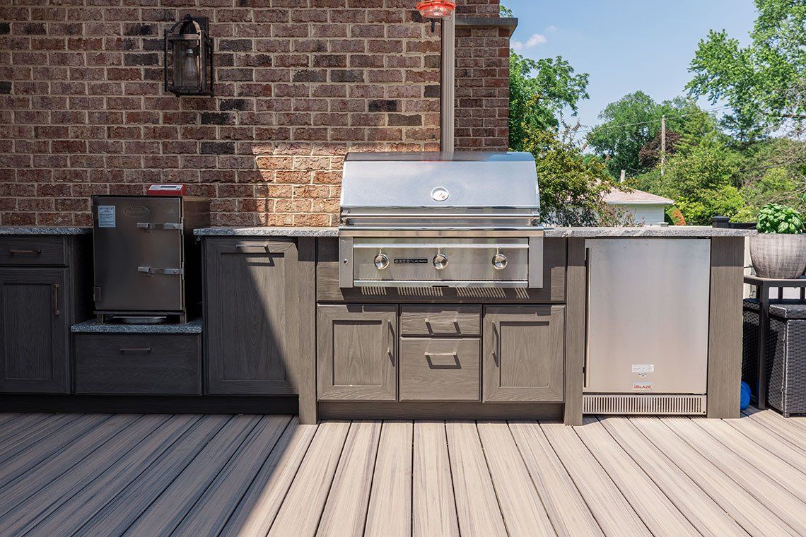 An outdoor kitchen with a grill and cabinets on a wooden deck.