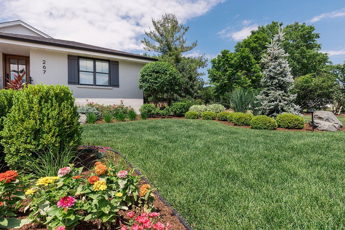 A white house with a lush green lawn and flowers in front of it.