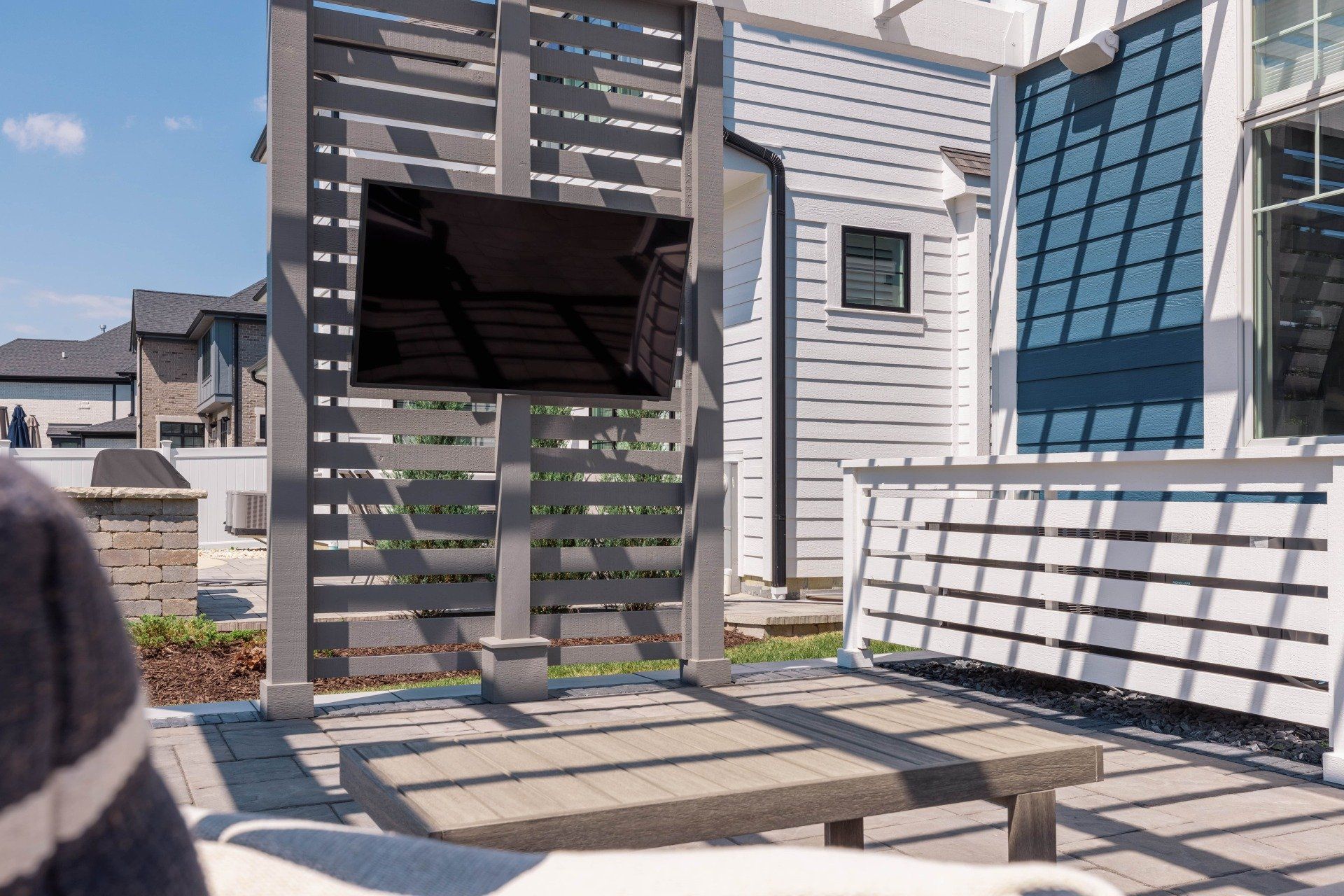 A patio with a table and chairs under a pergola in front of a house.