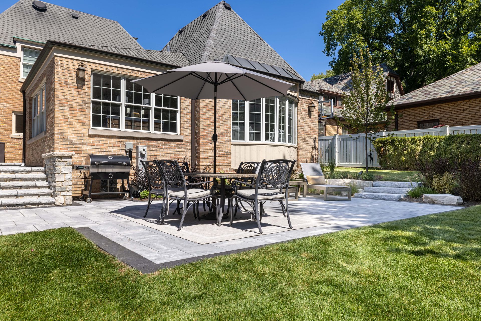 A patio with a table and chairs and an umbrella in front of a brick house.