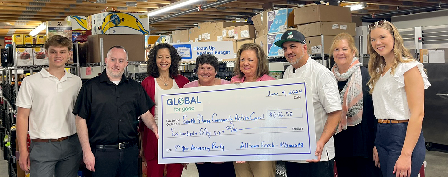 Group of people in a warehouse setting holding a large ceremonial check for a charitable donation.