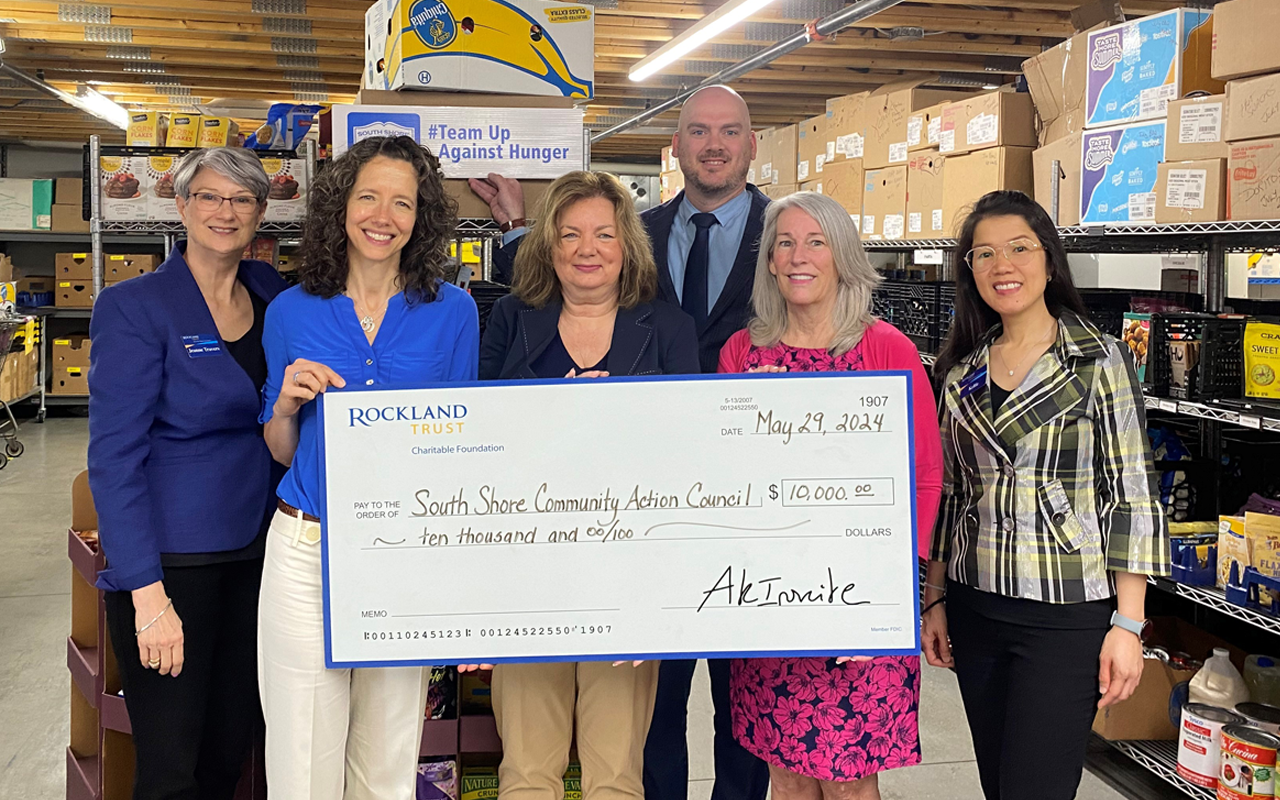Six people standing in a warehouse, holding a large ceremonial donation check for Santa State Community Food Center.