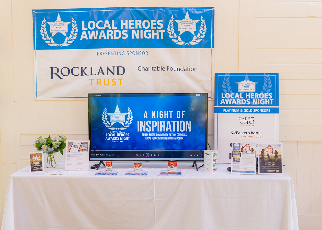 Local Heroes Awards display table with blue-and-white banners, TV screen, and event materials