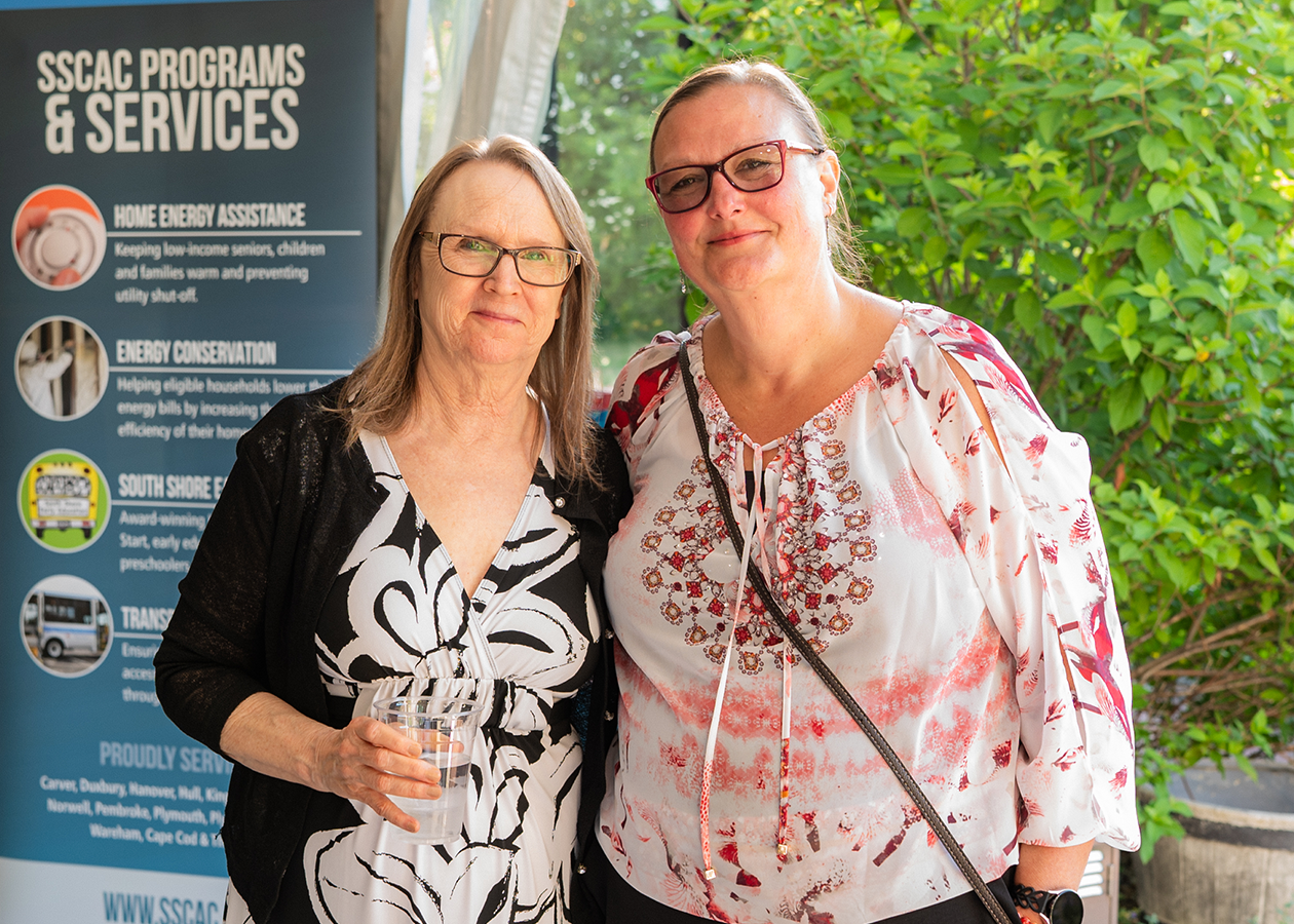Two women standing together smiling outdoors beside an SCCAC programs and services sign