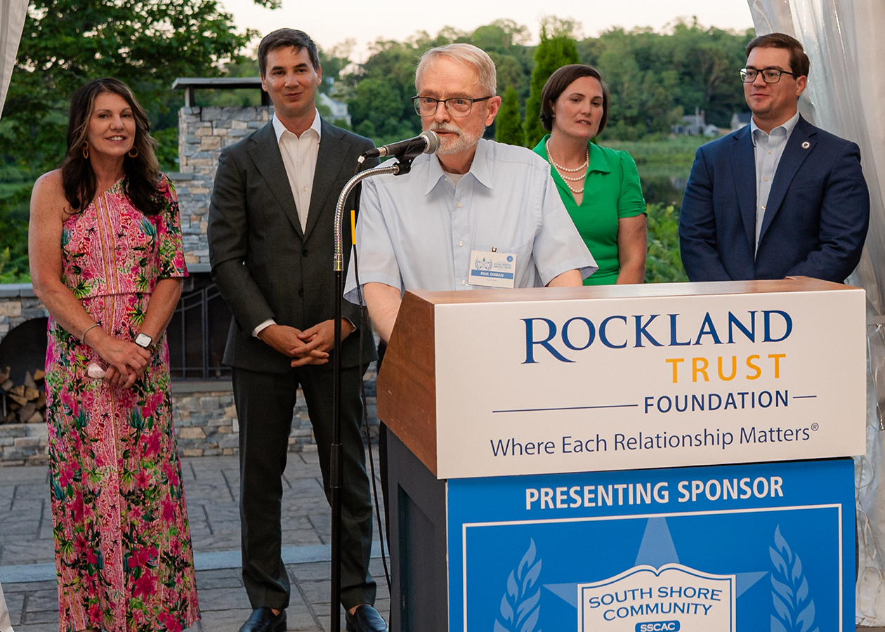 A man speaking at a podium with four people standing behind him outdoors