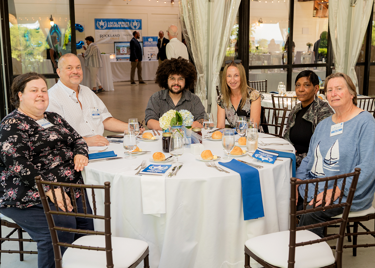 Five people seated at a round table in a decorated banquet hall, smiling at the camera.