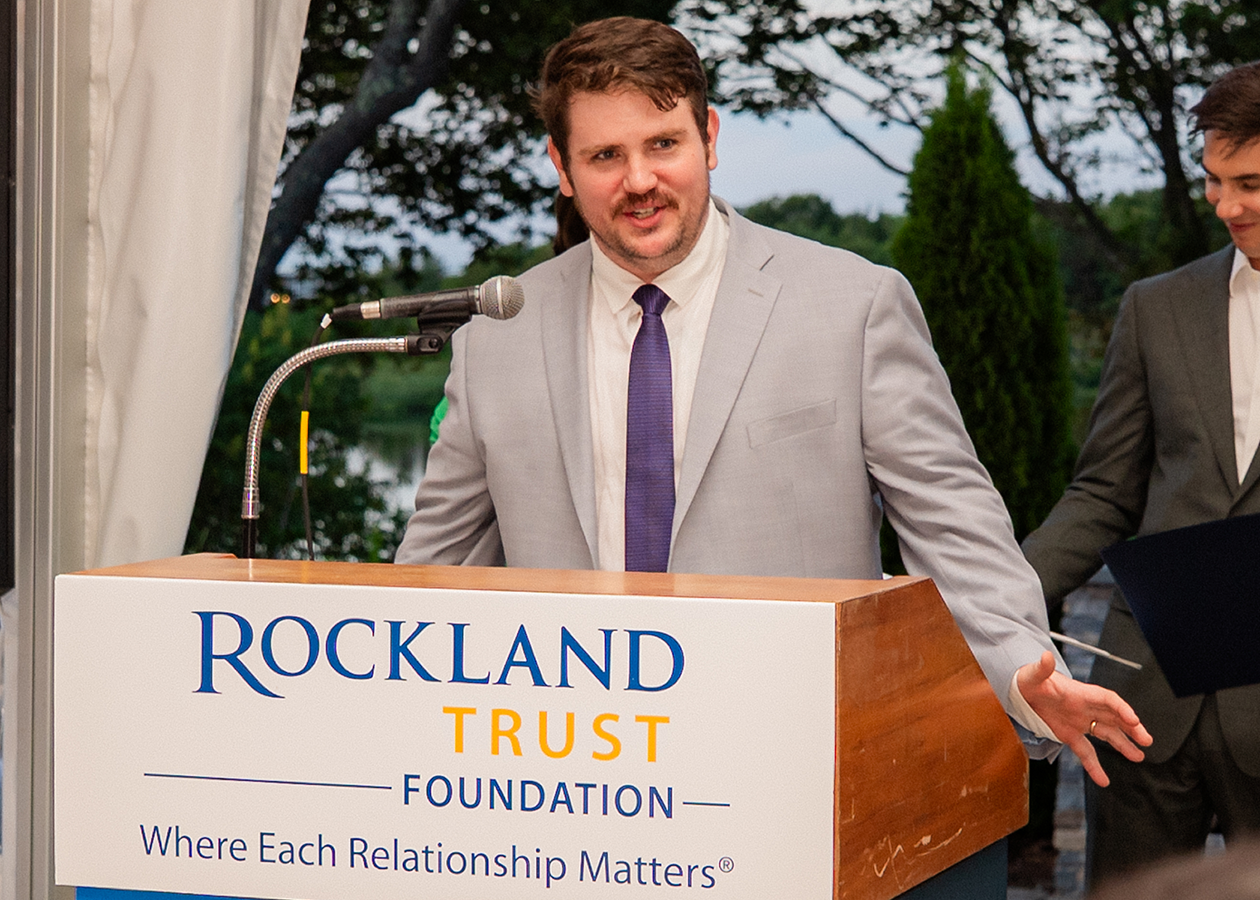 Man speaking at podium outdoors, with another man beside him