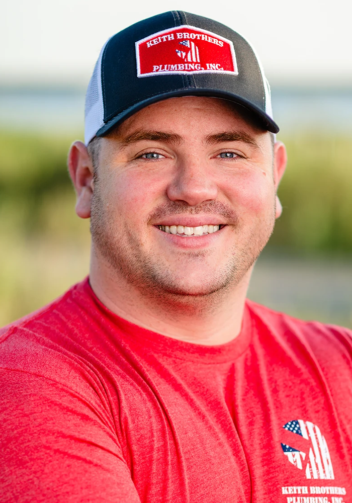 Smiling person in a red shirt and blue cap, standing outdoors in a field