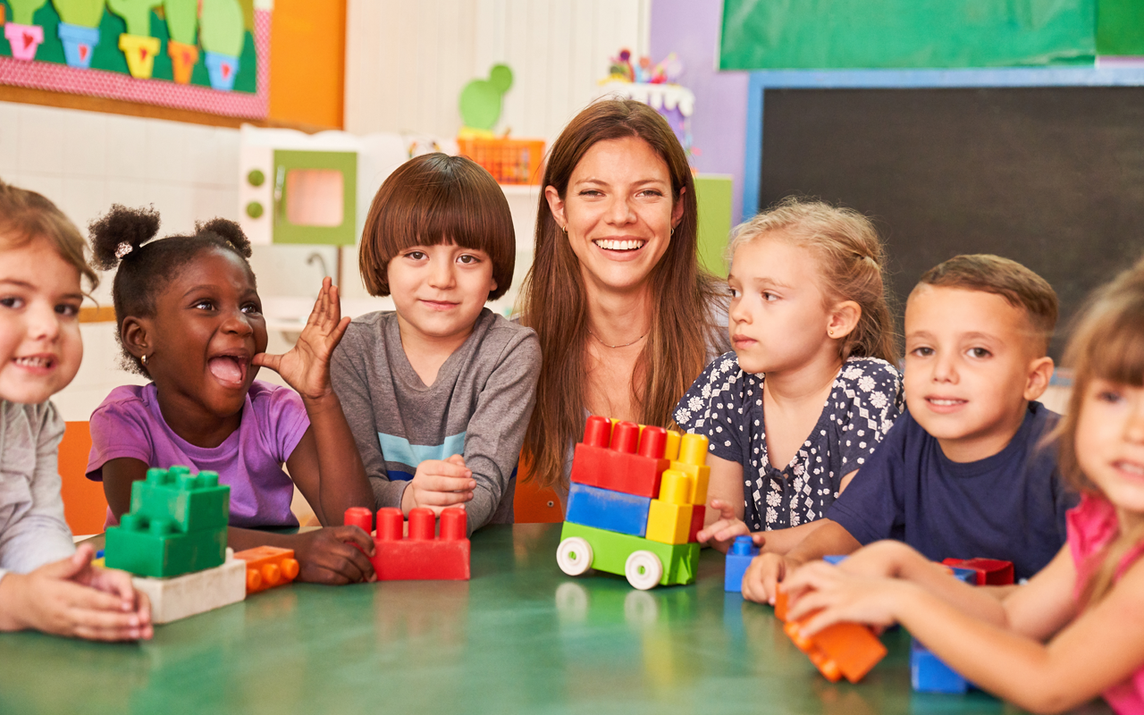 A teacher and group of students sitting at a table with colorful plastic building blocks in a classroom.