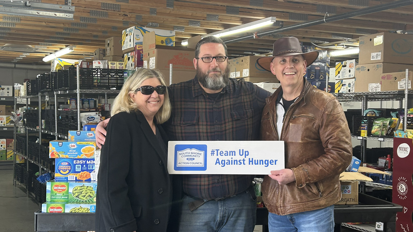 Three people stand in a warehouse holding a sign that reads