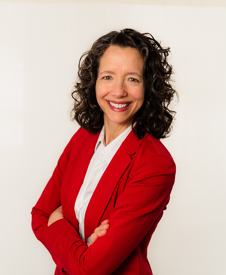 SSCAC CEO  in red blazer with arms crossed, smiling, in front of white backdrop.