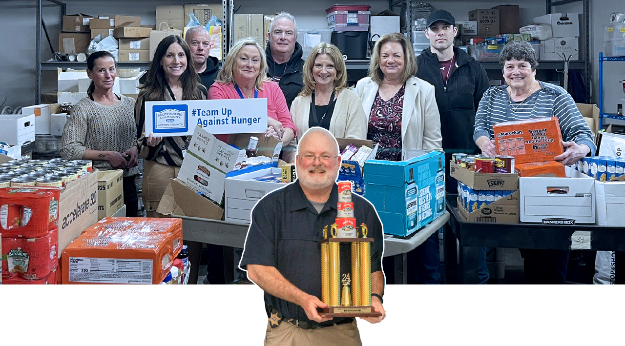 A group of people standing behind tables of donated goods, with one person in front holding a trophy in a warehouse.