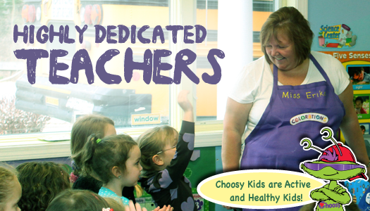 A teacher in a purple apron smiles at children in a classroom, with text reading