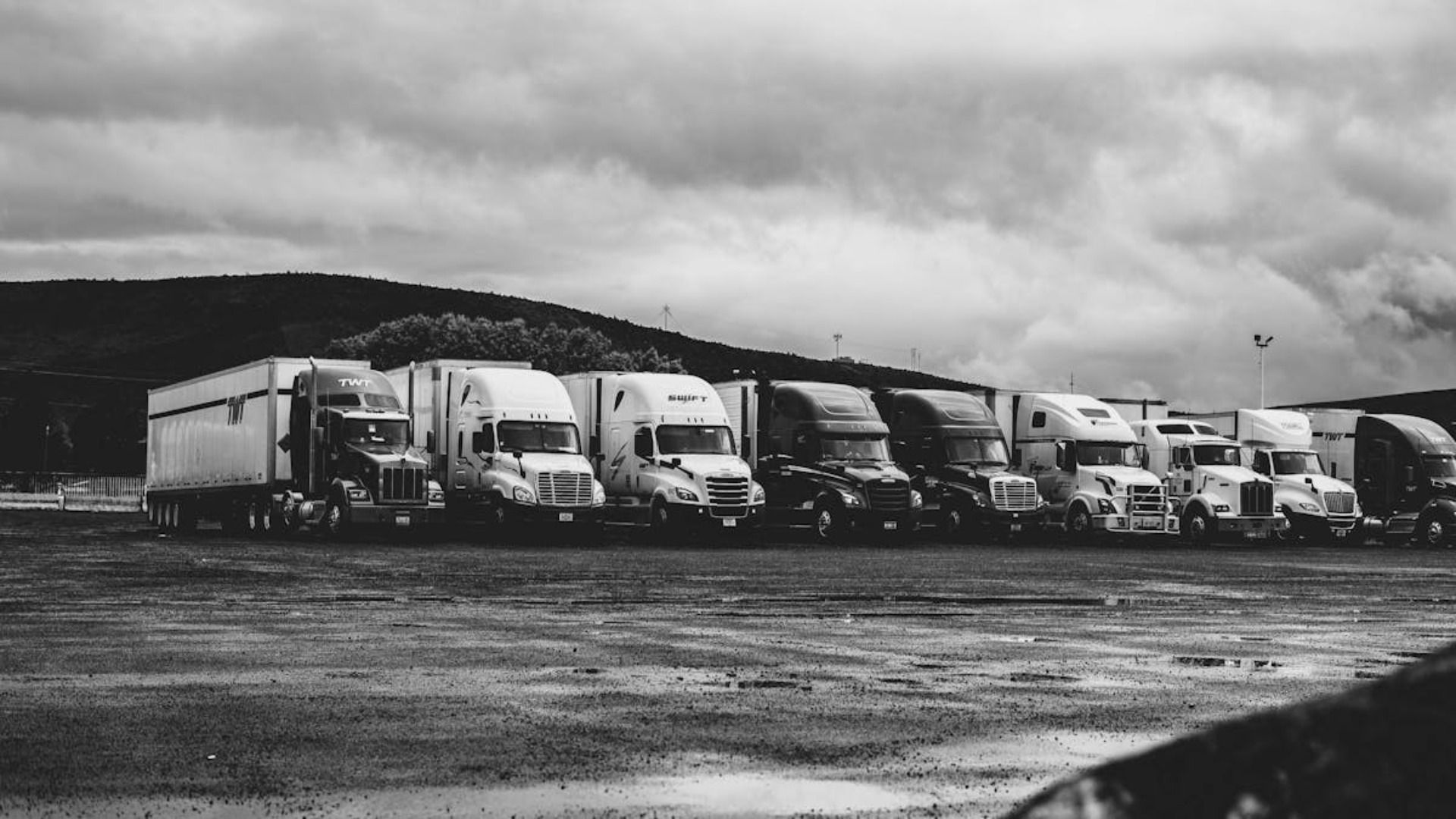 Una fotografía en blanco y negro de una fila de camiones semirremolque estacionados en un estacionamiento.