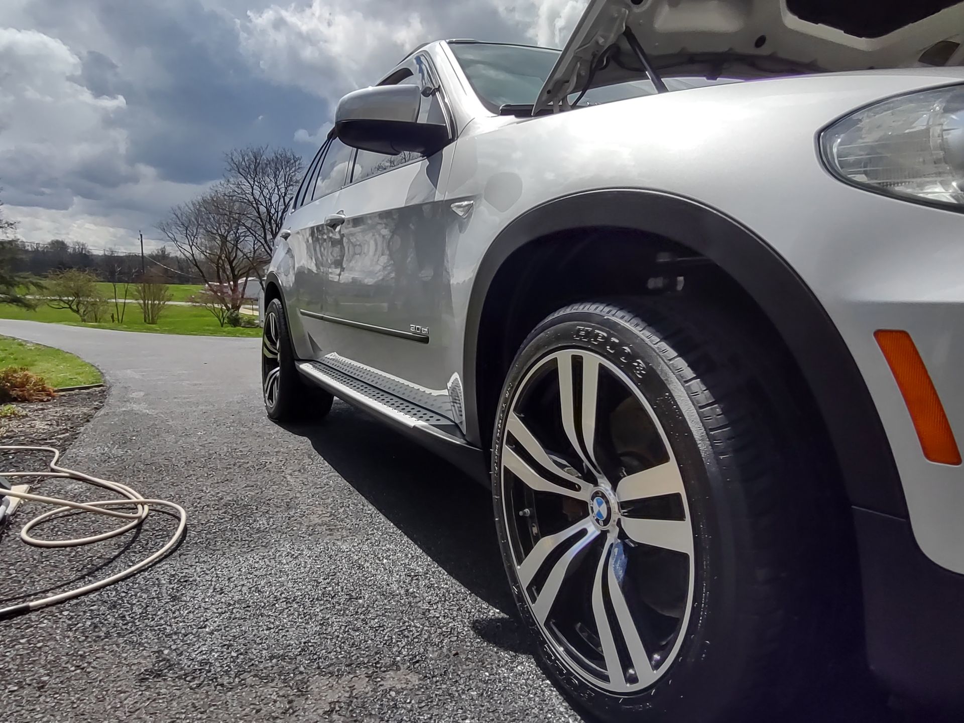 A silver car with the hood up is parked on the side of the road
