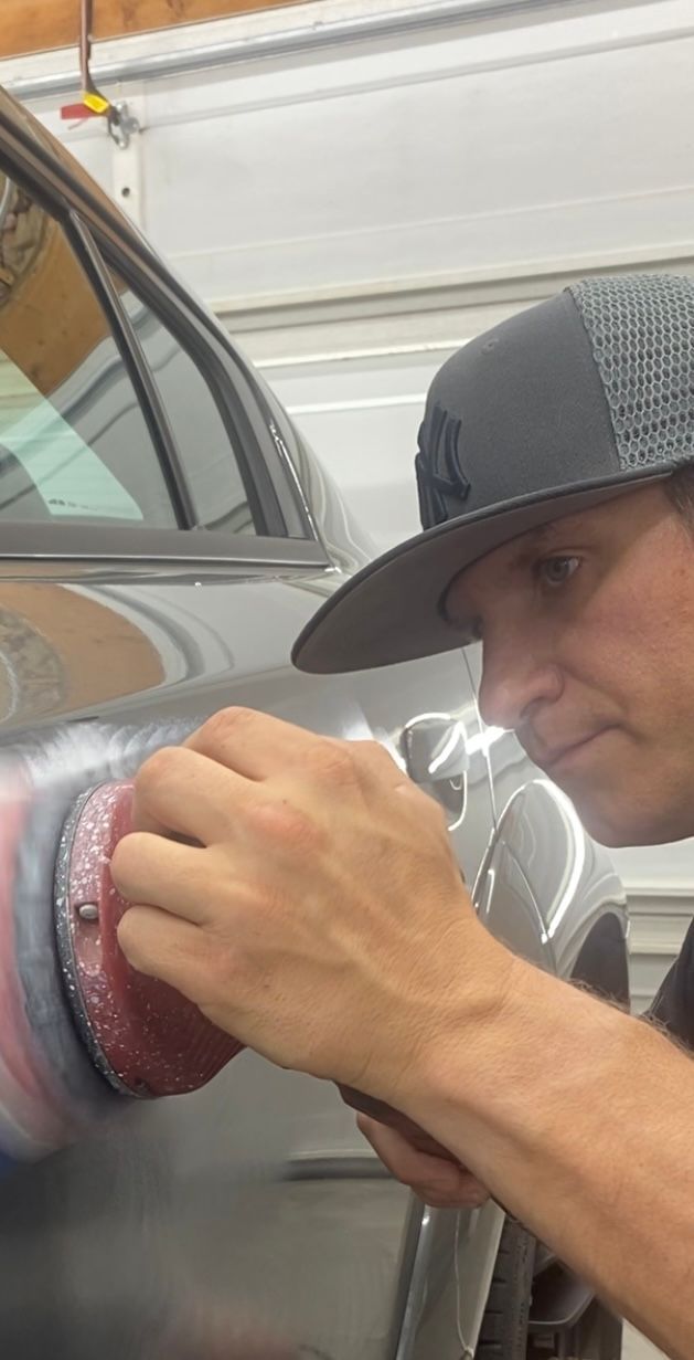 A man is looking at equipment while standing next to a black car