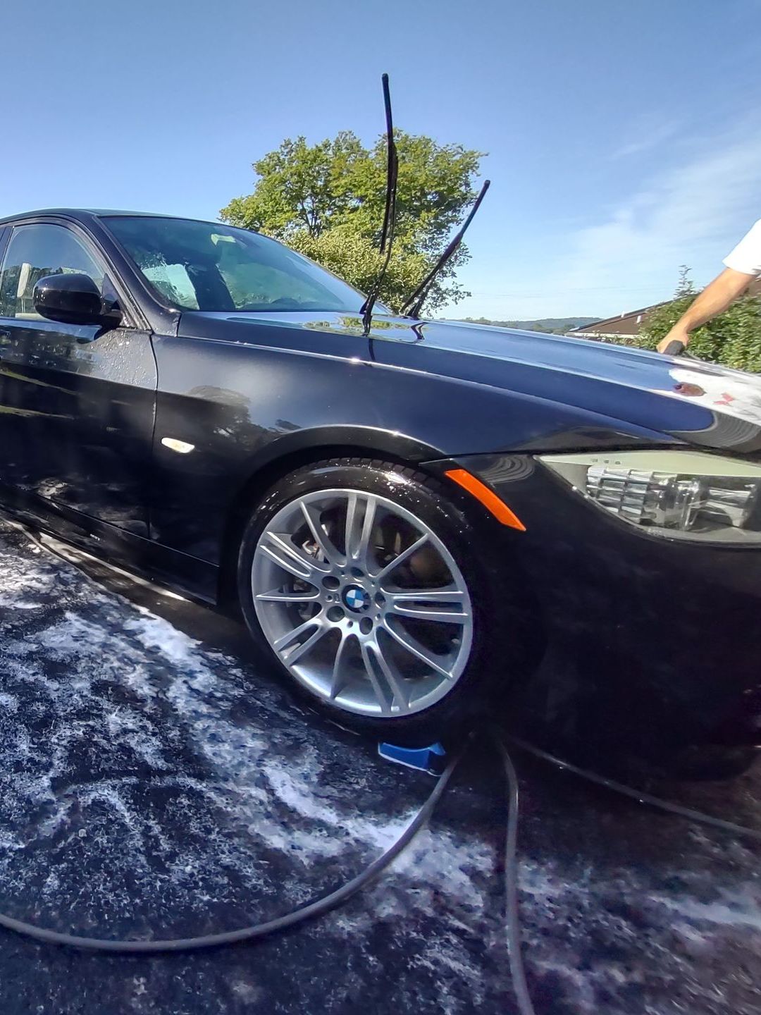 A man is washing a black bmw with a hose