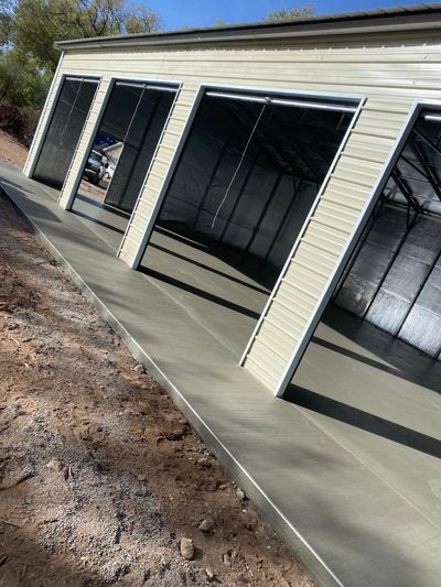Tilted view of a beige garage with open bay doors on a sloped concrete driveway under clear skies