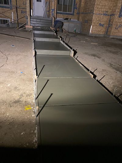 Concrete walkway under construction between stone walls, with rebar rods protruding along the edges.