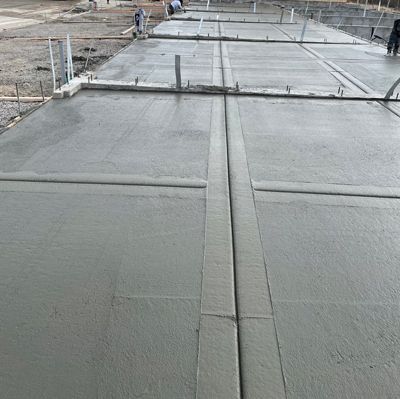 Freshly poured concrete slab with workers in the distance at a construction site
