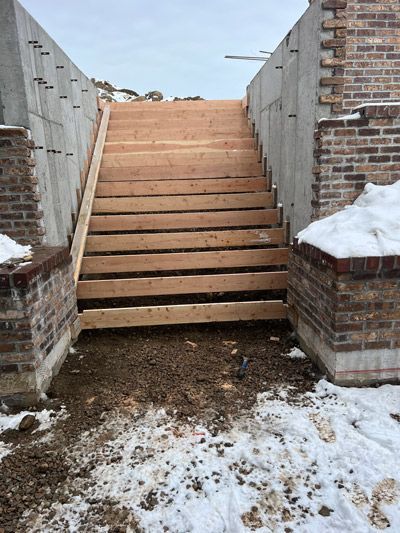 Wooden stairs between brick walls, with snow on the sides and dirt at the base.