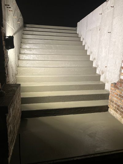Lit concrete stairway at night, flanked by white walls and brick sides, lit by a bright overhead light.