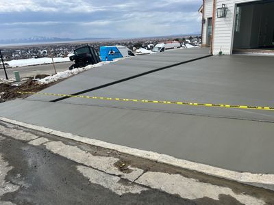Fresh concrete driveway beside a house, cordoned off with yellow caution tape in a snowy rural setting