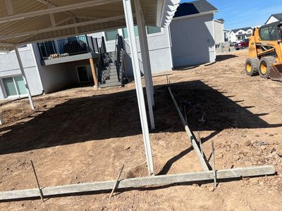 Construction site with dirt yard, house foundations, and a small loader under a partly built structure.