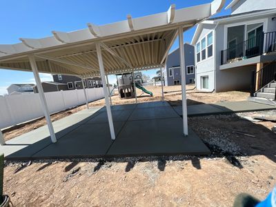 Covered carport beside modern homes with a white canopy over a concrete slab and dirt foreground
