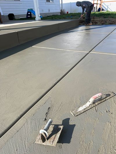 Freshly smoothed concrete driveway with trowels in foreground and a worker finishing the edge in the background