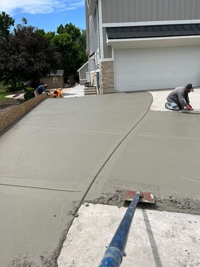 Workers smoothing fresh concrete driveway beside a garage, with a blue tool pole in the foreground.