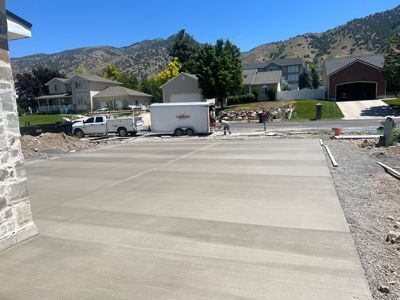 Wide concrete driveway in a suburban neighborhood with a white truck, trailer, and houses in the background