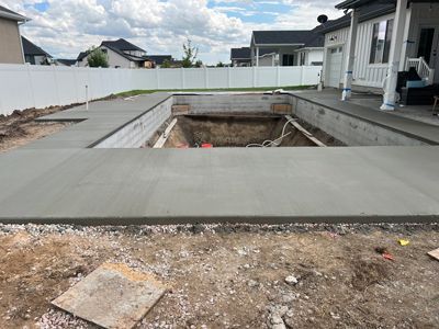 Concrete backyard pool deck with a large unfinished rectangular pool excavation in the center