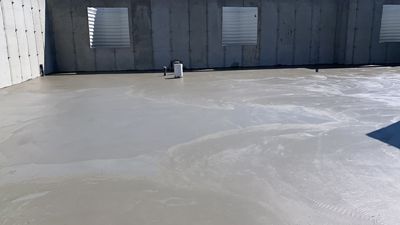 Empty concrete lot in front of a dark industrial building with two vented doors.